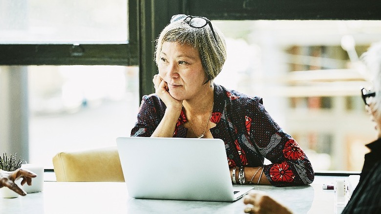 Older woman with eyeglasses on her head listens during a meeting