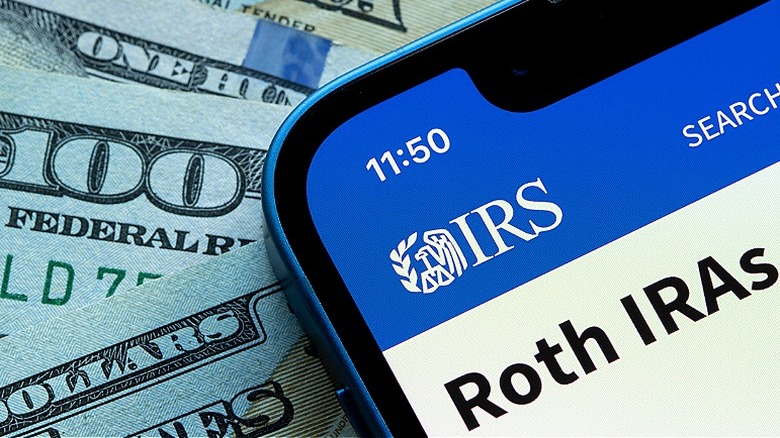 $100s bills next to the Roth IRAs page on the IRS website on smartphone