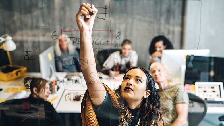 View of a team meeting with one person writing on a transparent board