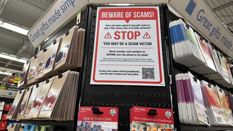 A display of gift cards in a store with a sign warning of the possibility of being scammed.