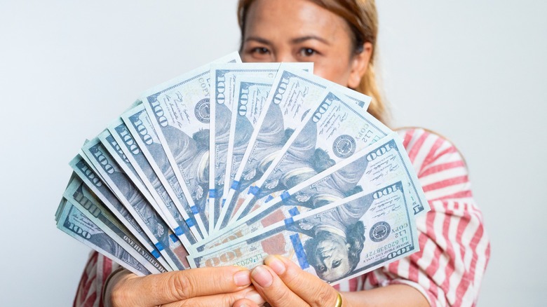 A woman holding several hundred dollar bills in a fan