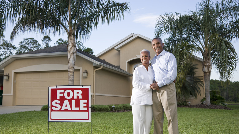 Happy older couple next to for sale sign