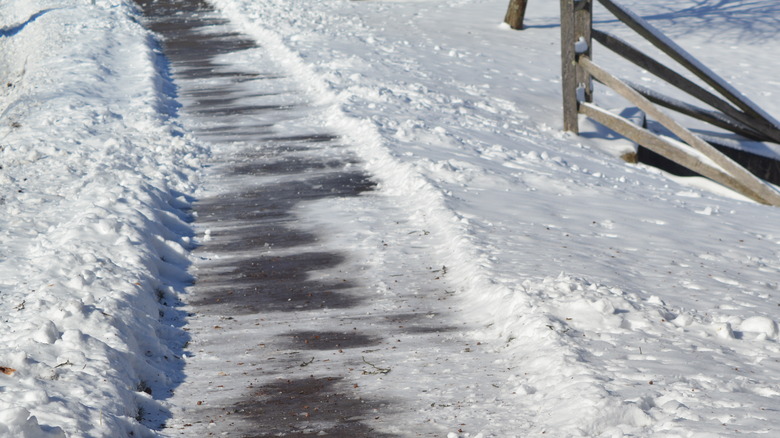 Bits of dirt and snow remain on cleared sidewalk by broken fence