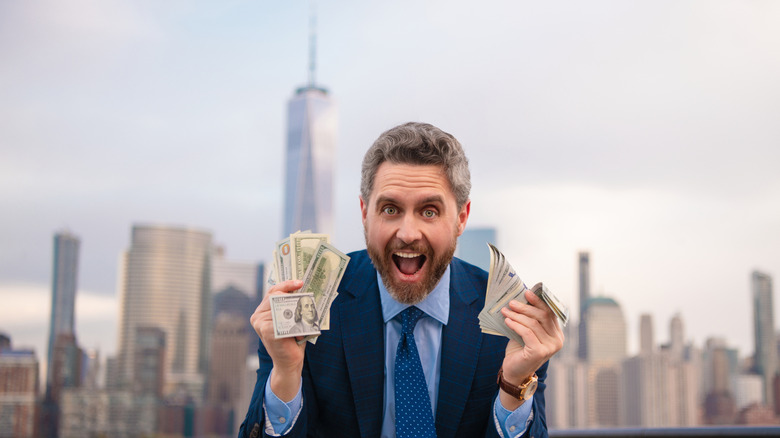 An excited man in a suit holding cash in front of the New York skyline