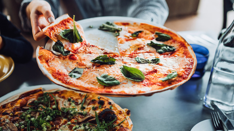 A young woman getting a slice of freshly made pizza.