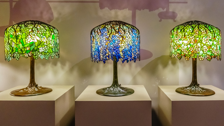 A trio of genuine Wisteria Tiffany lamps on display in a museum, two green, one blue.