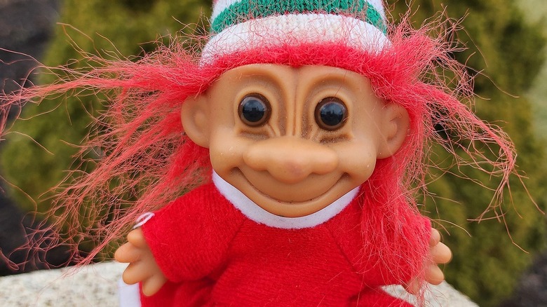 Troll doll wearing red sweater and green-and-white-striped hat while sitting outside