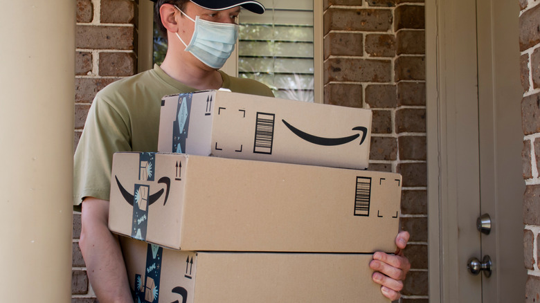 A man wearing a face mask carrying Amazon delivery boxes