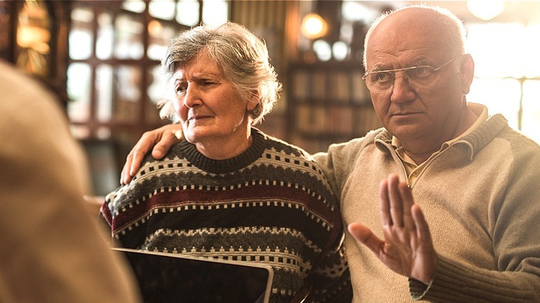 Couple talking with unseen person; the husband holds hand up indicating 'no'