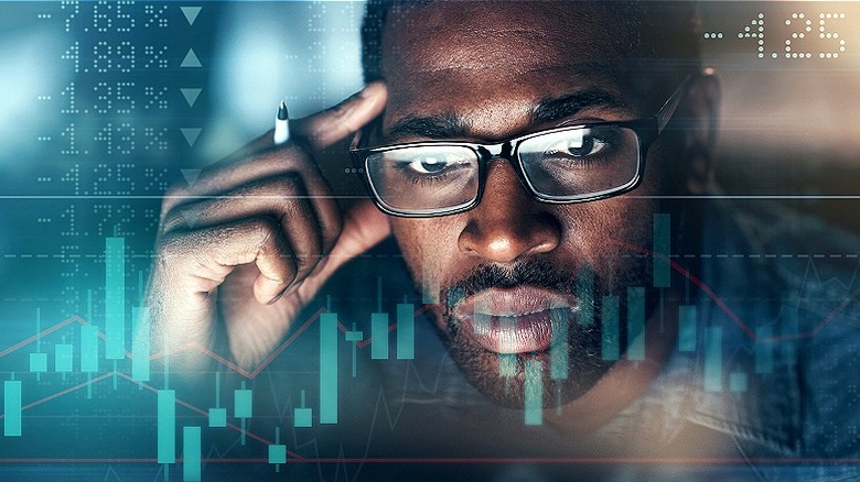 Man with glasses looking intently at stock charts and prices