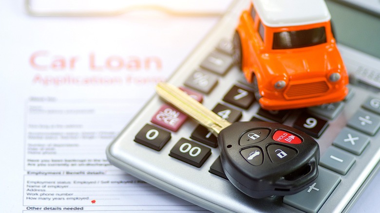 A model car and car key sit atop a calculator and car loan application