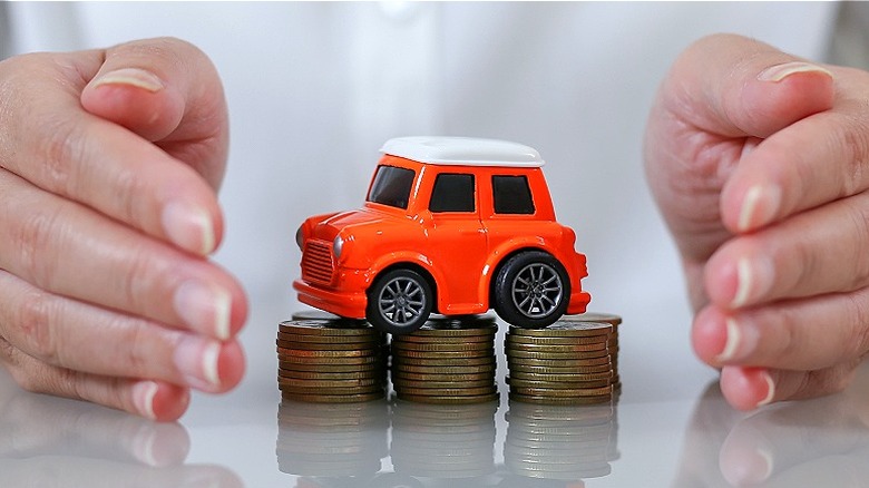 A person holds their hands around model car and coin stacks