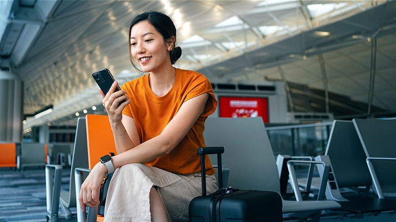 Woman smiling, checking phone at airport