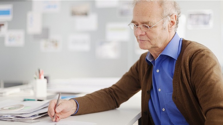 An older man writing while in an office